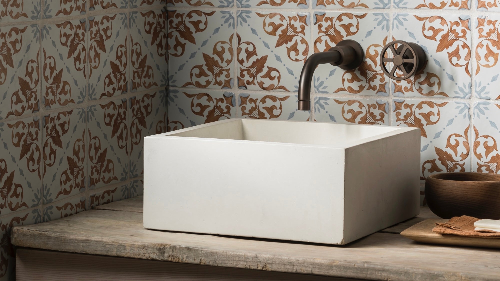 Concrete basin set against some hand painted tiles used as a splash back and brass taps 