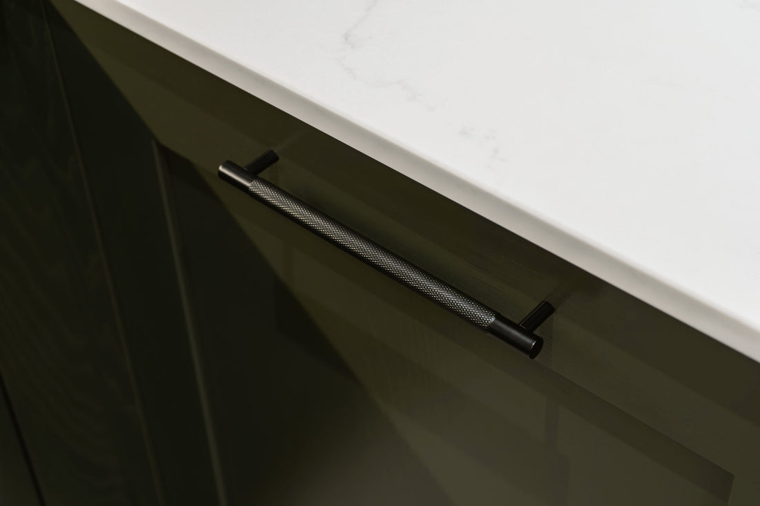 Knurled black cabinet pull attached to a dark green shaker style kitchen cabinet with marble worktop