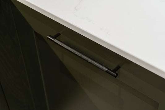 Knurled black cabinet pull attached to a dark green shaker style kitchen cabinet with marble worktop