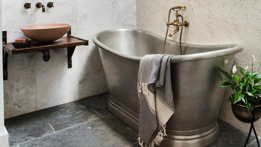 Tin bathtub paired with antique brass freestanding taps and a pink concrete basin 