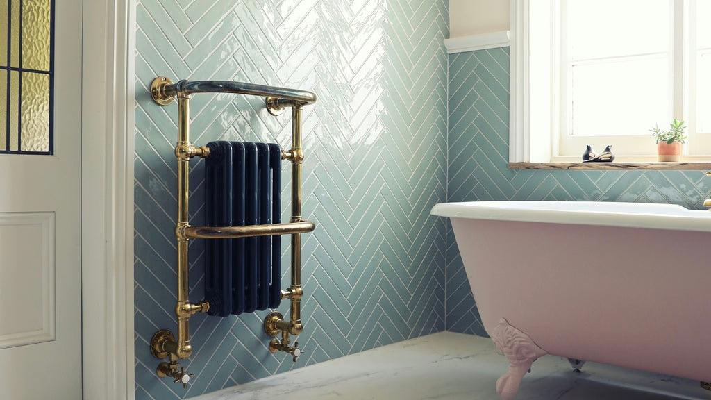 Gold heated towel radiator in modern bathroom with green metro tiles and a pink claw foot bathtub